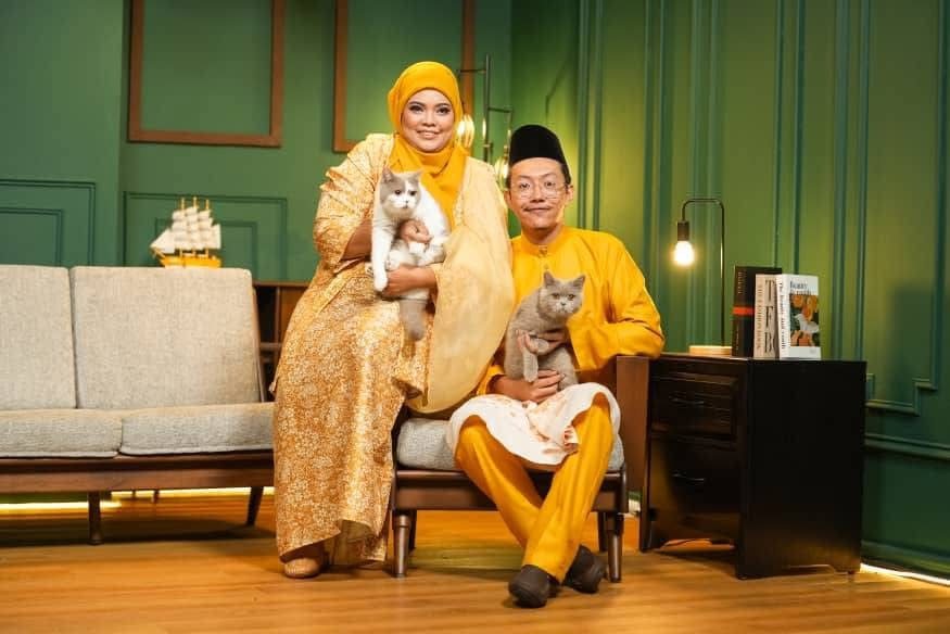 Siti and Syahmin seated in matching yellow traditional outfits, each holding a British cat